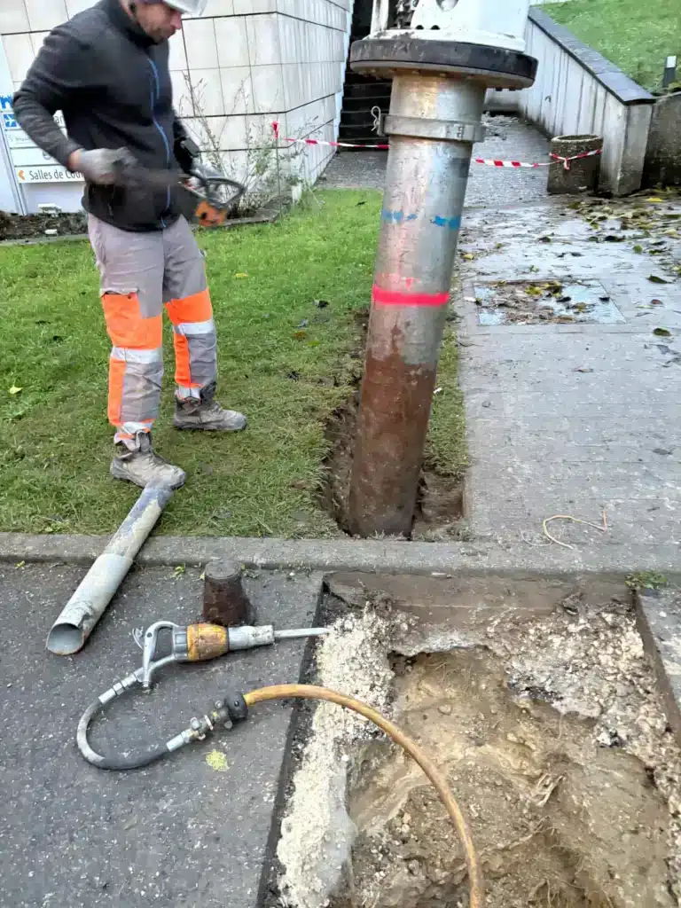 Ouvrier utilisant une tronçonneuse près d'un pilier et marteau-piqueur sur un chantier de voirie.