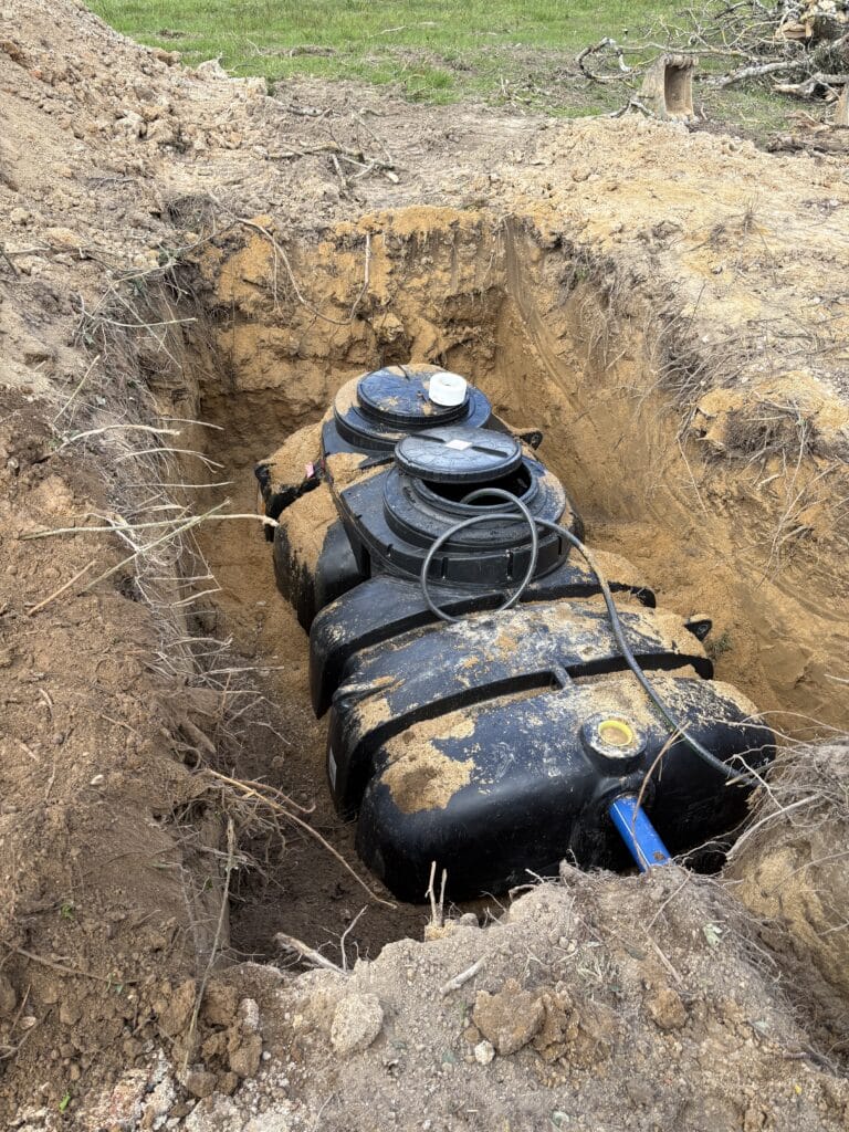 Fosse septique : installation du réservoir en plastique Installation d'une fosse septique en plastique noir dans une excavation de terre avec tuyau bleu.